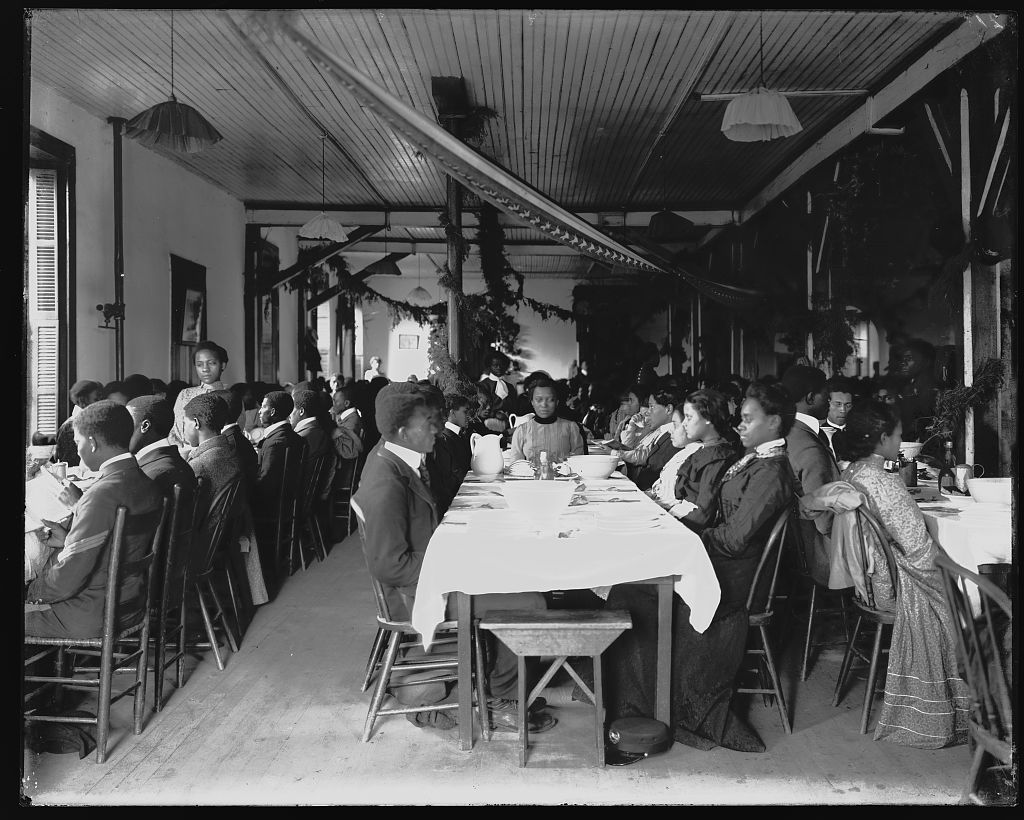 Interior view of dining hall, decorated for the holidays, with students sitting at tables at the Tuskegee Institute